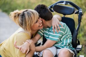 joyful woman hugging a boy in wheel chair for article by kelley way titled Should I Create a Special Needs Trust?