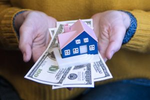 hands holding us dollars and a tiny house for article by kelley way attorney about will prop 19 affect property taxes california walnut creek