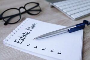 A estate plan checklist on a pad of paper with glasses, keyboard and a pen for blog article titled by kelley way: what documents should be in every estate plan