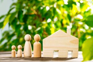 wooden family and house figures on a table with a green foliage background featured image for the article by kelley way titled How Often Should I Update My Estate Plan