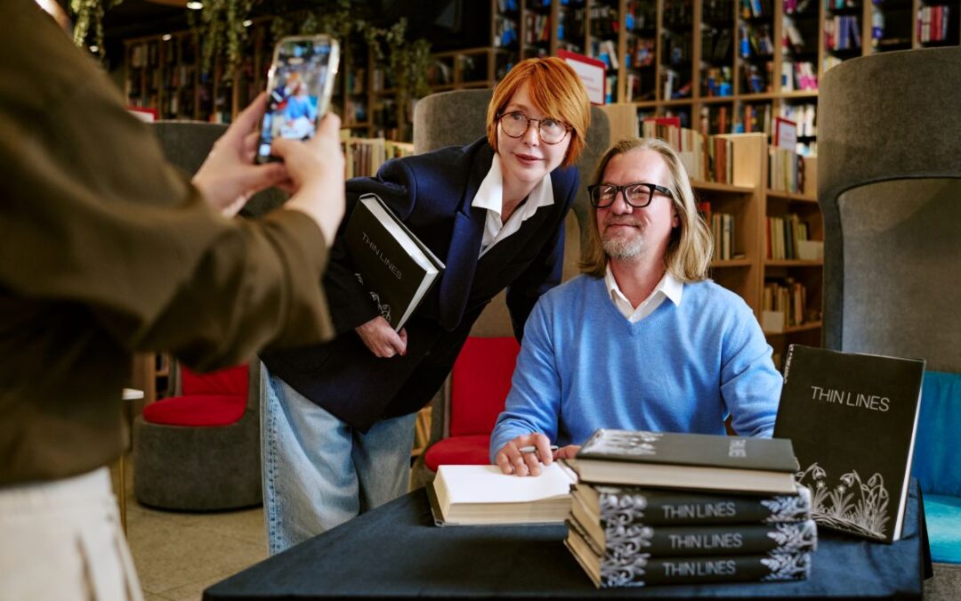 Author Signing Books While Being Photographed for blog article by kelley way titled Brand Protection 101: A Checklist for Self-Published Authors
